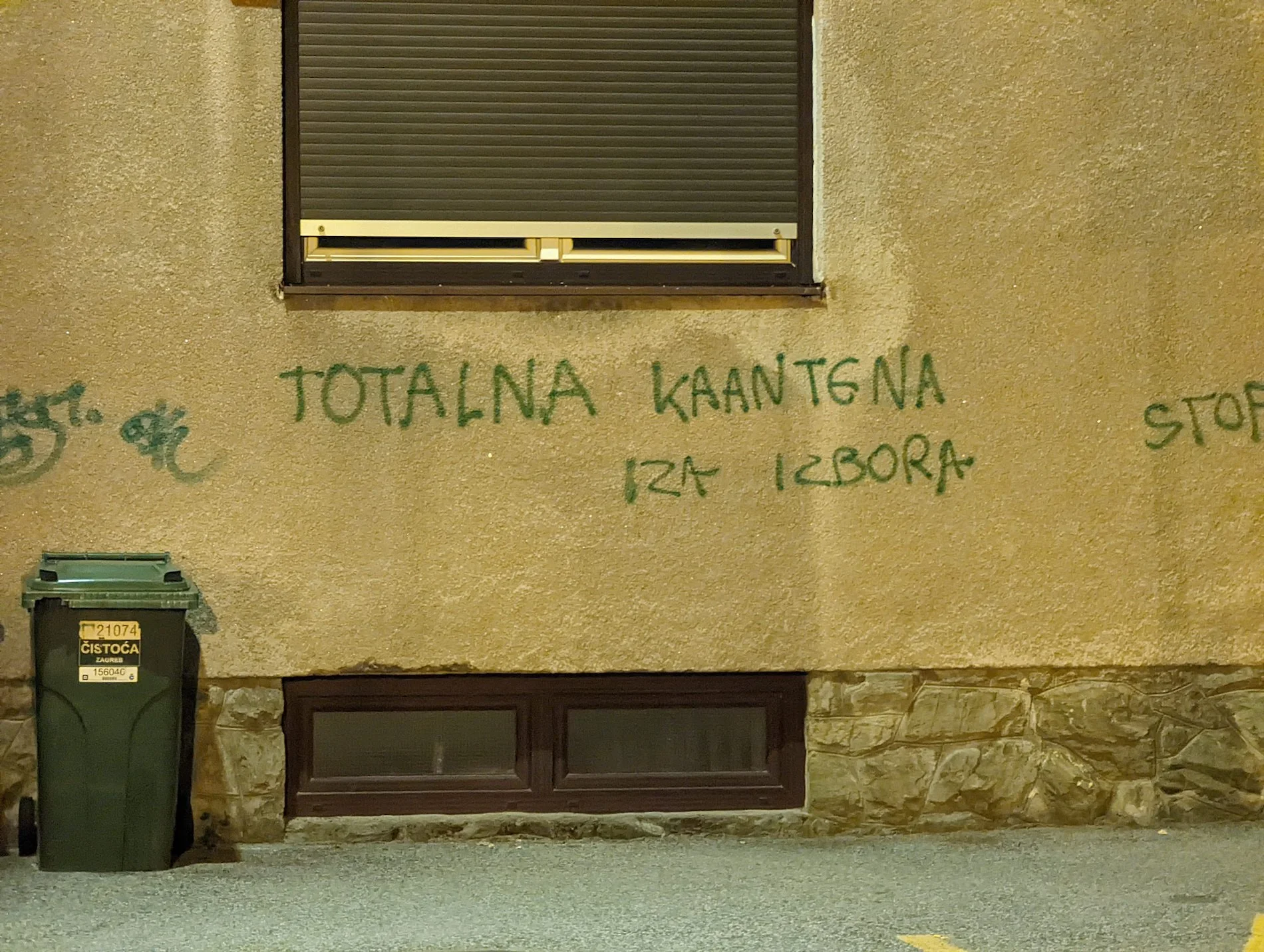 A picture of protest grafitti on a building in Zagreb during the COVID pandemic. It says 'totalna kaantena iza izbora' in all-caps green spray writing, meaning 'total quarantine after the elections' with a glaring typo in quarantine ('karantena')